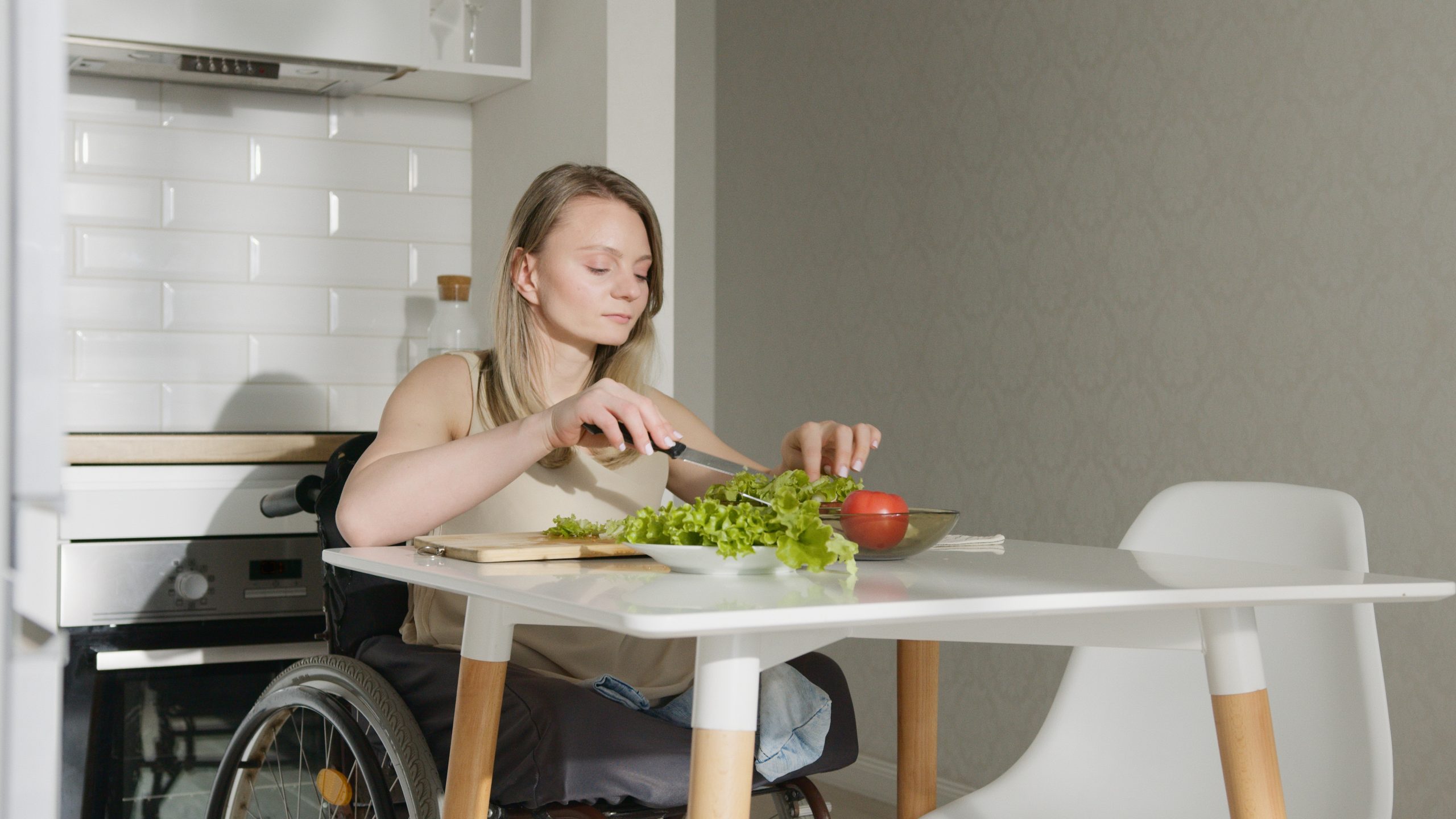 pexels-artem-podrez-7495749 A woman in a wheelchair cuts vegetables at her kitchen table