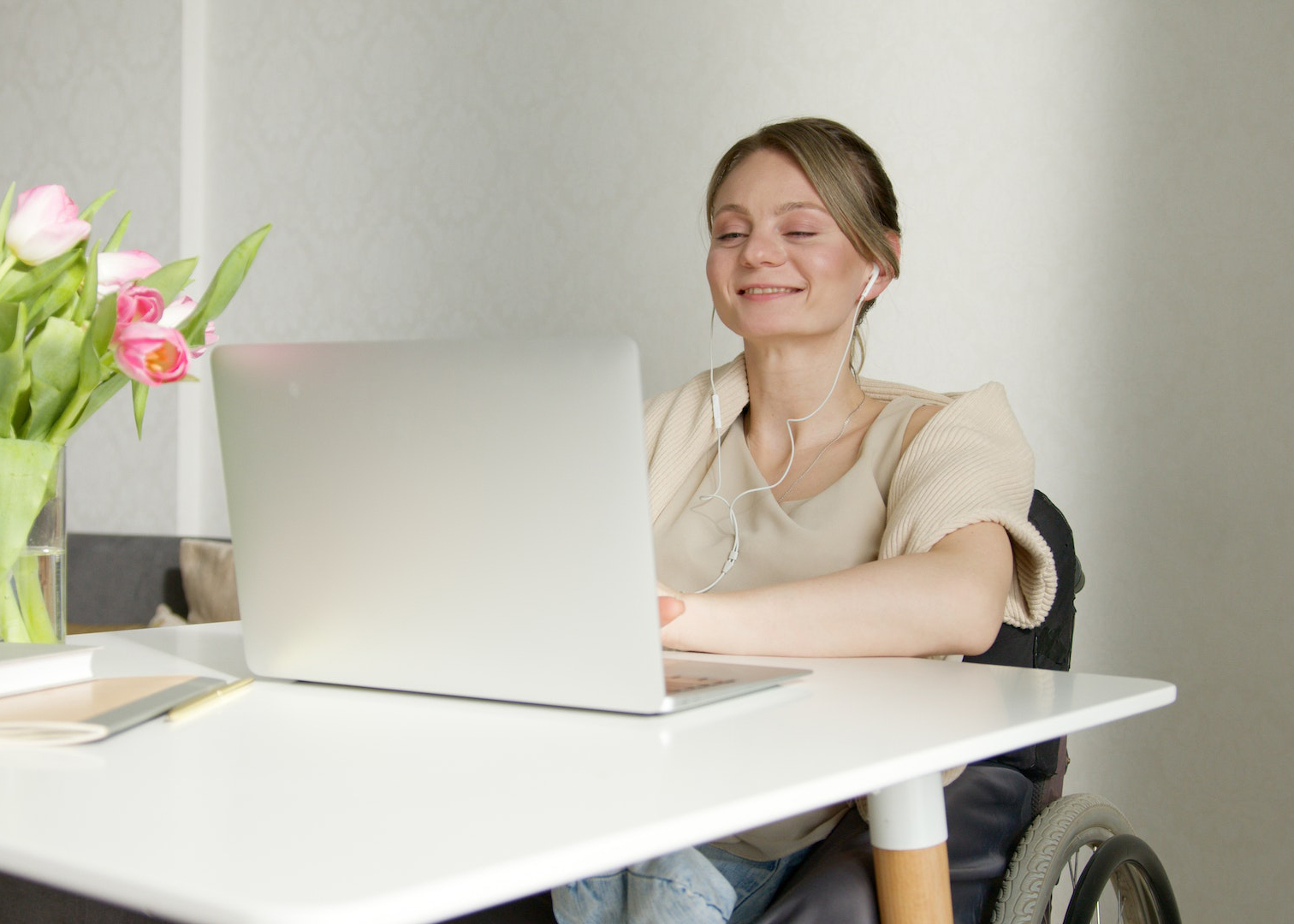 pexels-artem-podrez-7495877 A woman in a wheelchair wearing earbuds smiles as she watches an online course on her computer