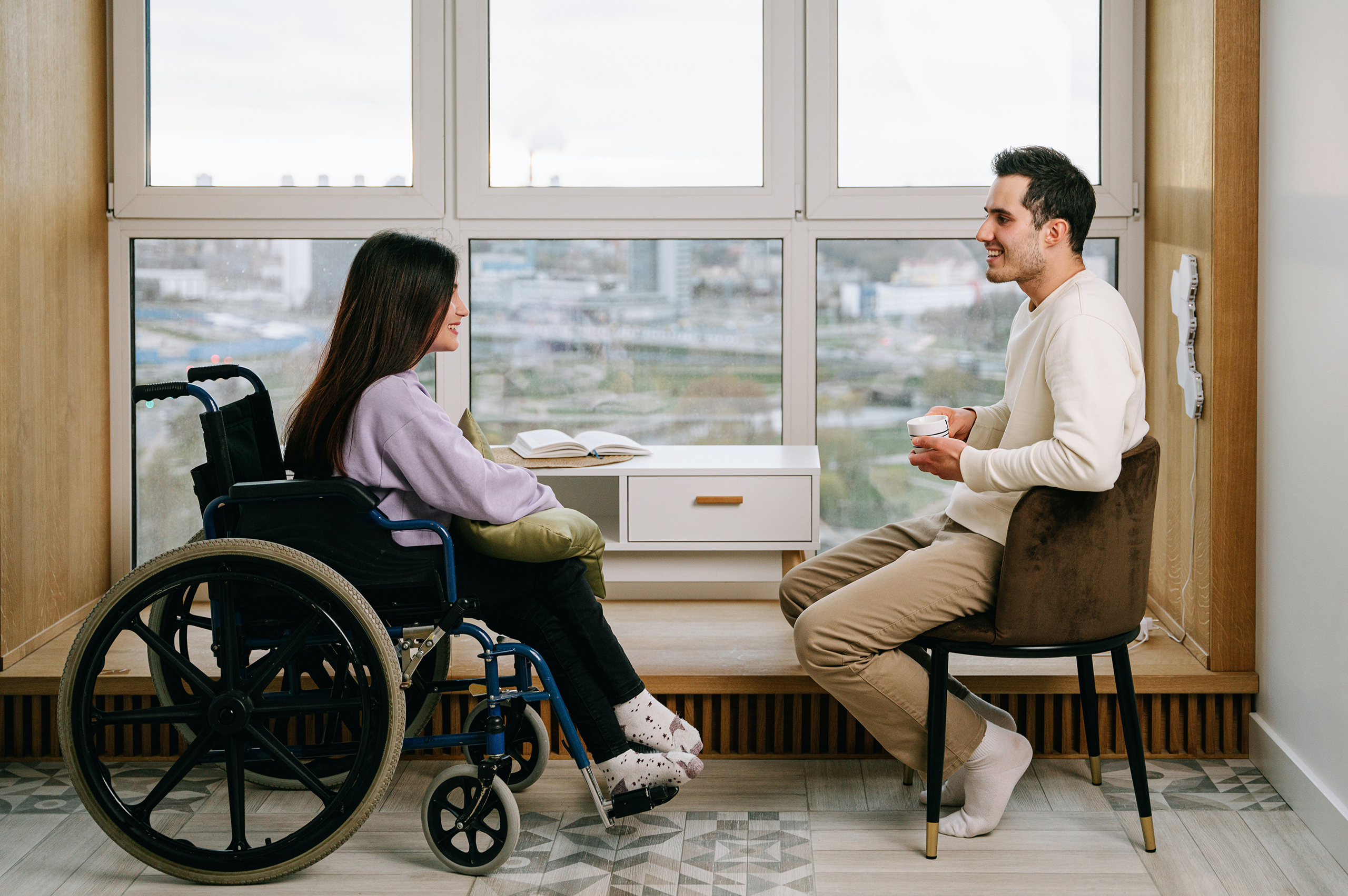 pexels-ivan-samkov-8127424 A woman in a wheelchair and a man in a chair have a conversation next to a window
