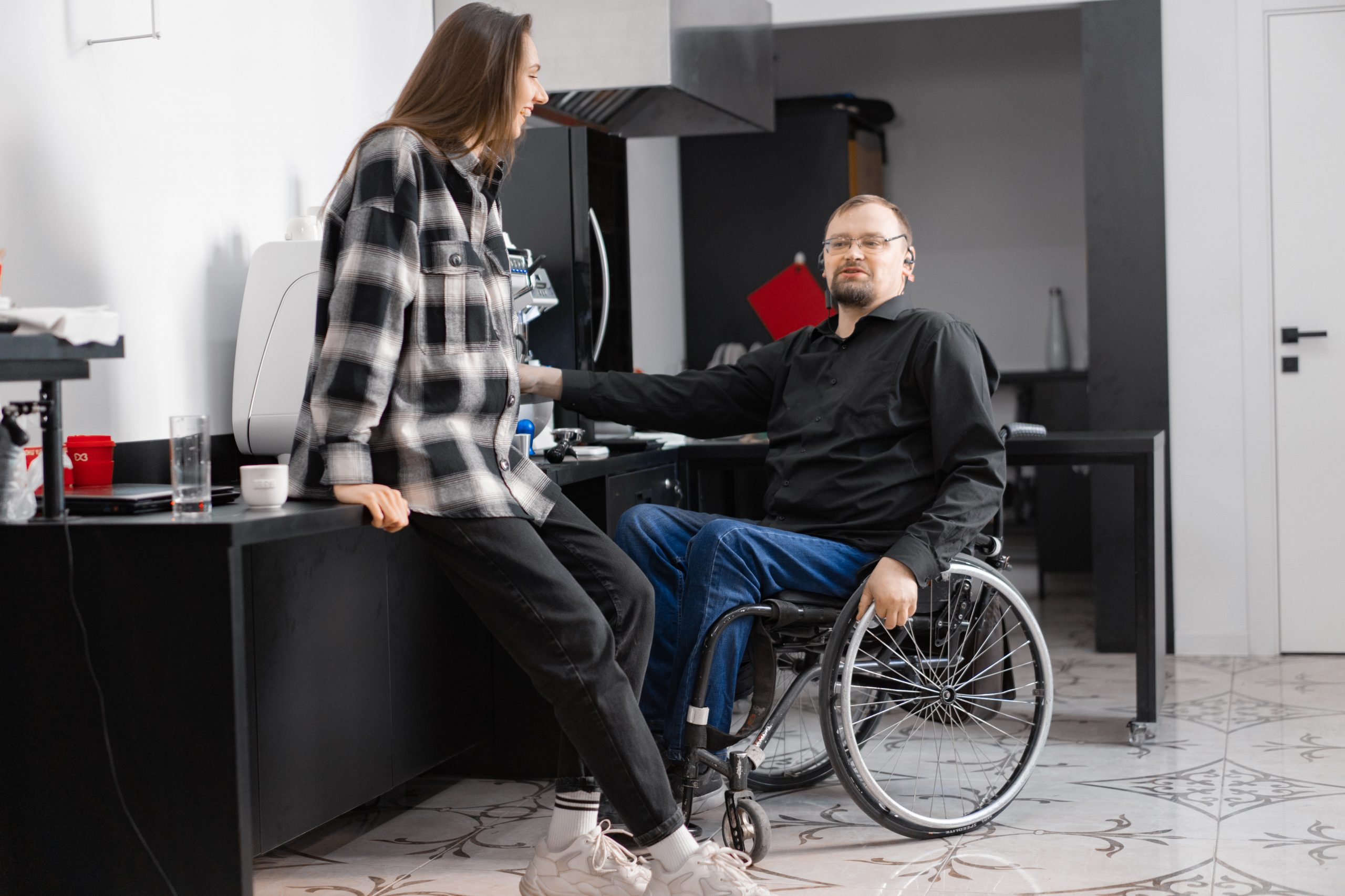 pexels-mikhail-nilov-7698032 A woman leans against a cabinet while talking with a man in a wheelchair