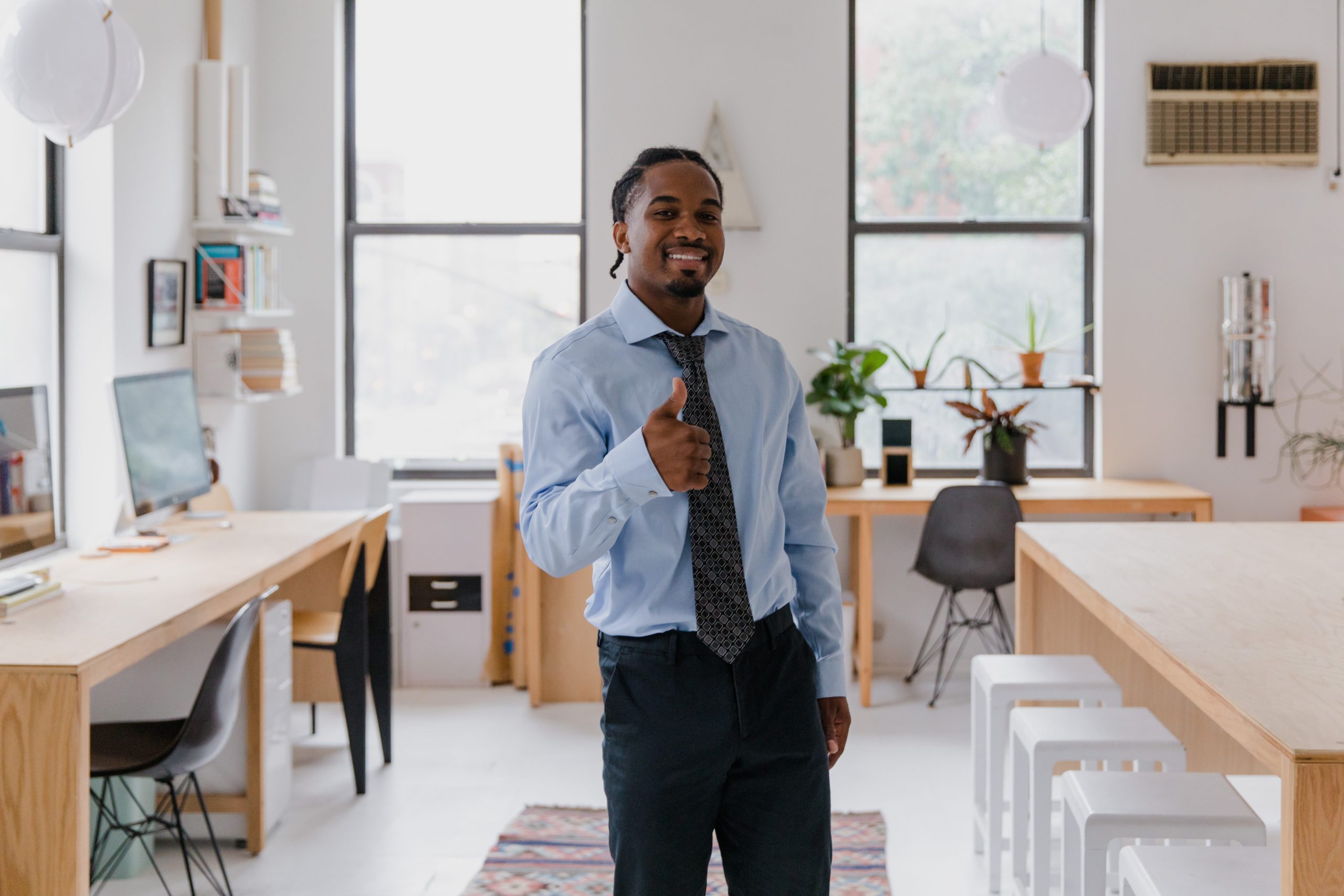 pexels-rodnae-productions-10029848 A man standing in an office smiles and gives a thumbs-up sign